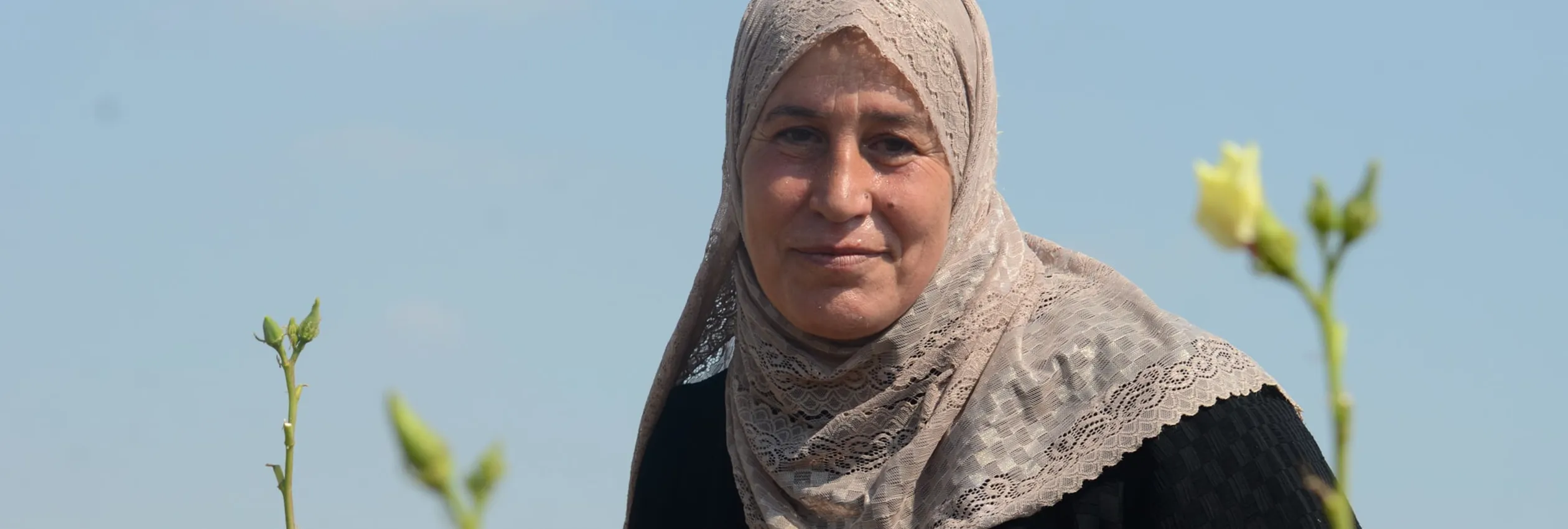Portrait of Syrian refugee Layla amongst okra flowers.
