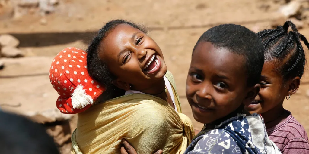 A young girl, carrying her doll on her back, laughs at the camera at Kakuma refugee camp in the north-westerm region of Kenya.